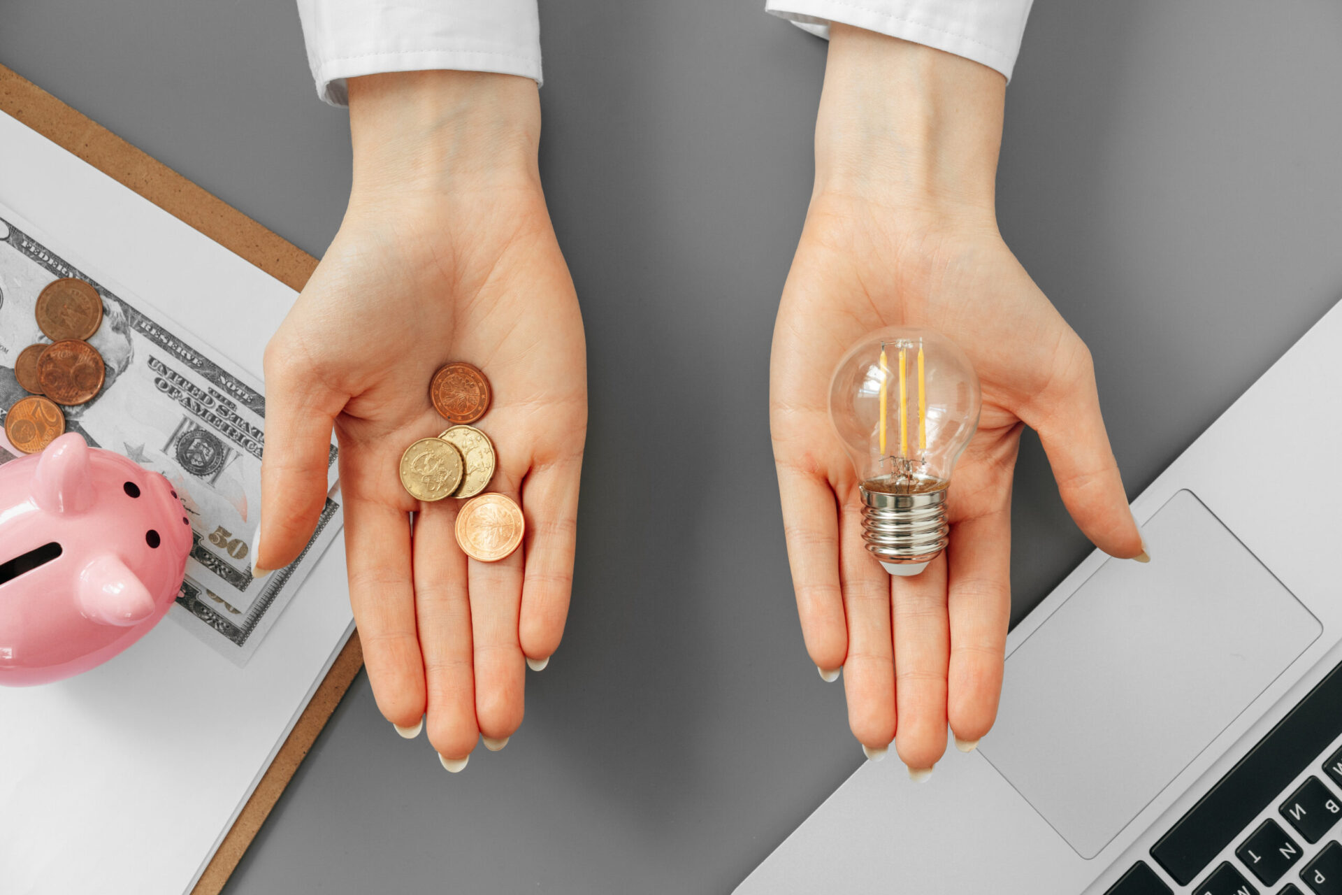 female hand holding a light bulb above the table on one hand and some cents on the other hand