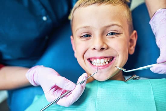 A kid beaming with a smile while sitting on a dental chair. The Dentist's hands are seen inspecting him.